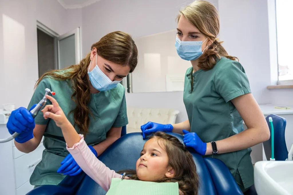 two young beautiful dentists girl in masks and gloves clean the baby's mouth.
