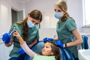 two young beautiful dentists girl in masks and gloves clean the baby's mouth.