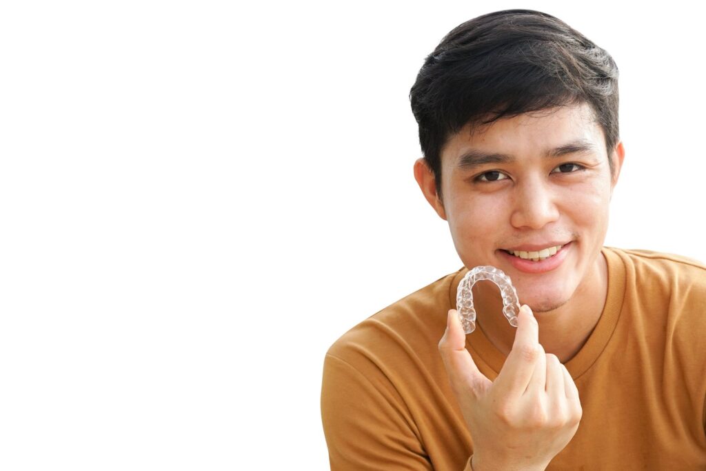 Teenage patient holding a clear Invisalign aligner and smiling